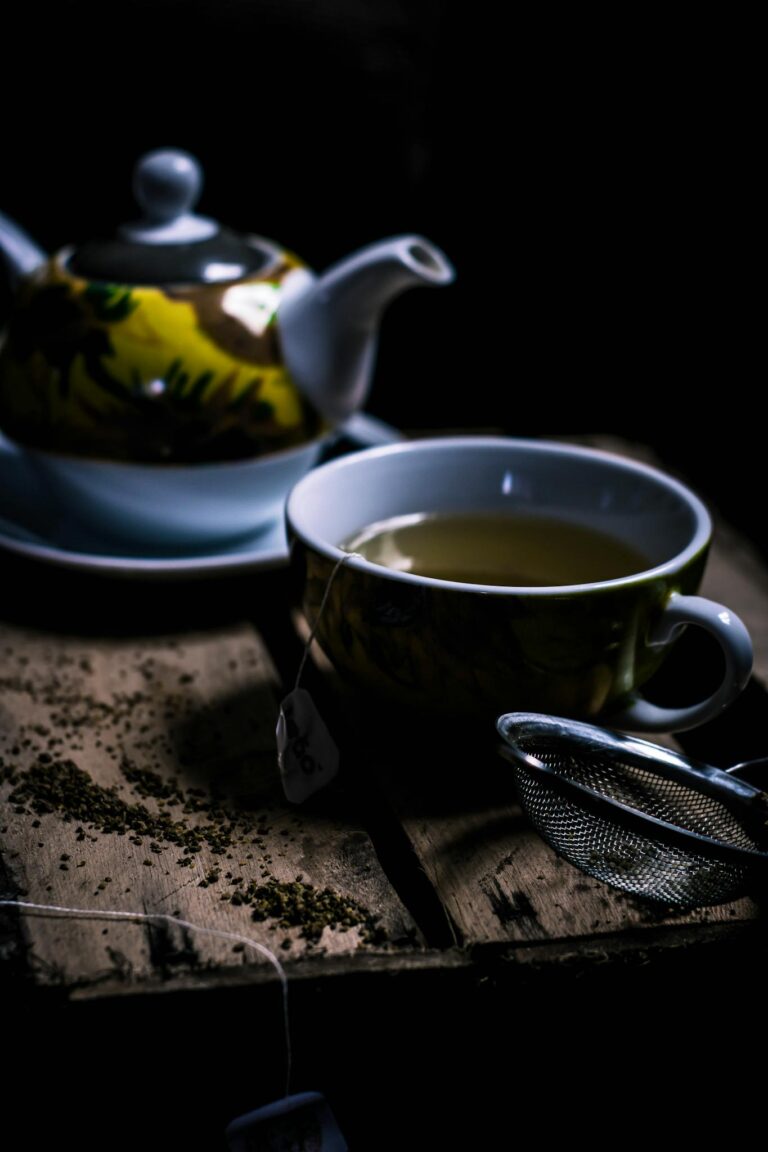 A cozy dark wooden setup with green tea in a teacup, teapot, and strainer.