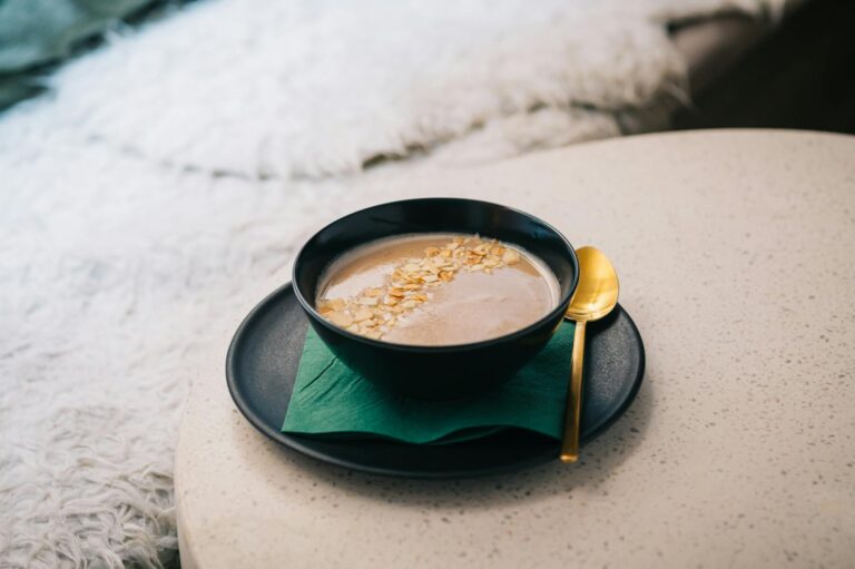 A stylish black bowl of creamy oatmeal topped with sliced almonds and a golden spoon.