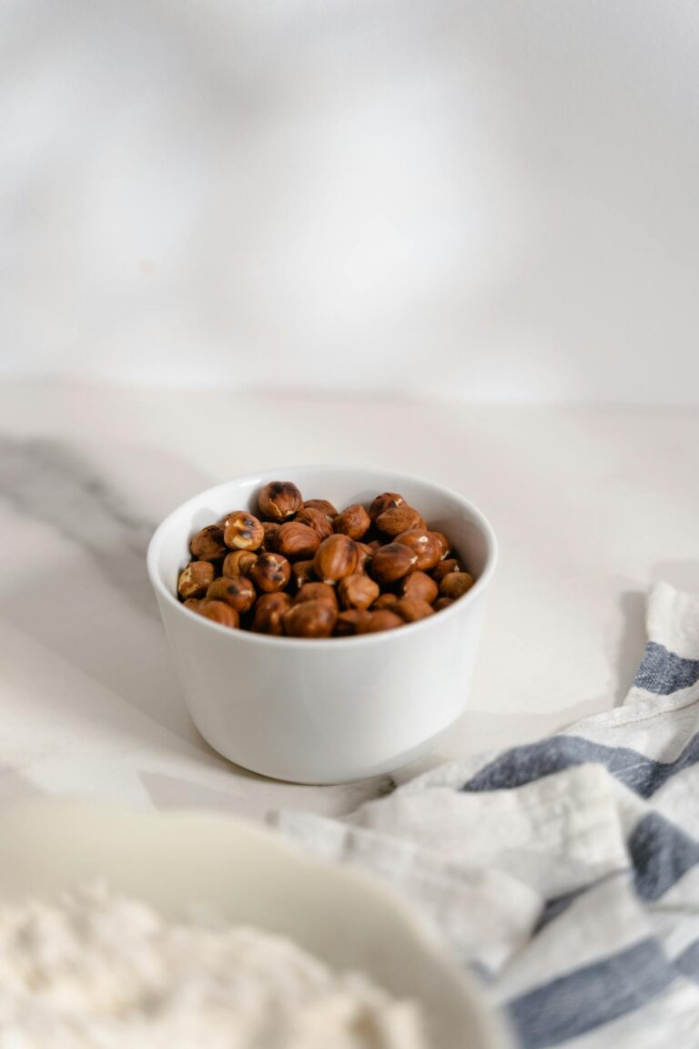 A white bowl filled with hazelnuts on a marble surface, perfect for culinary and nut-themed visuals.