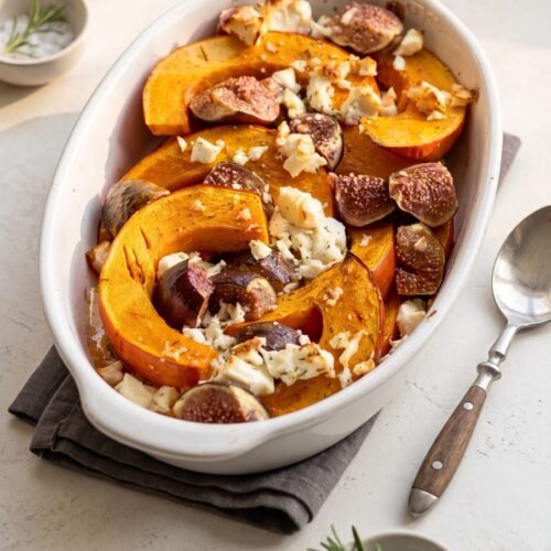 Gebackene orange Kürbisspalten in einer ovalen Auflaufform, belegt mit geviertelten Feigen und zerbröseltem Feta.